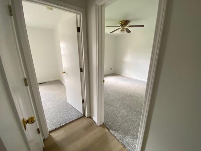 hallway with light colored carpet and light wood-style flooring