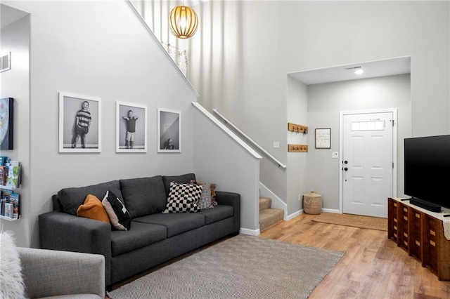 living area featuring stairs, a high ceiling, light wood-style floors, and baseboards