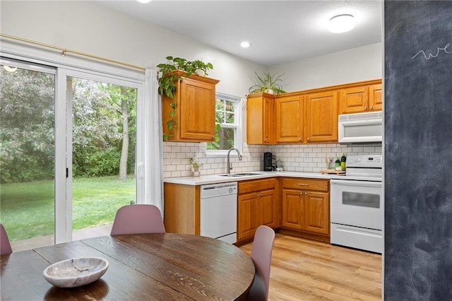 kitchen with white appliances, a sink, backsplash, light countertops, and brown cabinetry