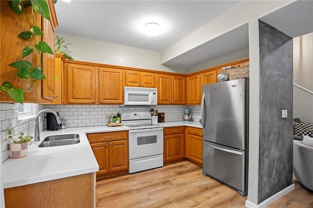kitchen featuring white appliances, a sink, brown cabinetry, light wood-style flooring, and backsplash