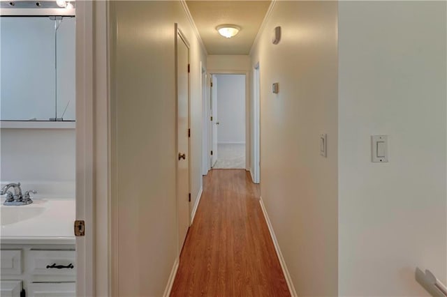 hall with light wood-type flooring, baseboards, and a sink