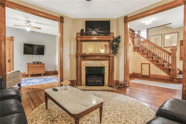 living room with hardwood / wood-style flooring, baseboards, stairway, a ceiling fan, and a glass covered fireplace