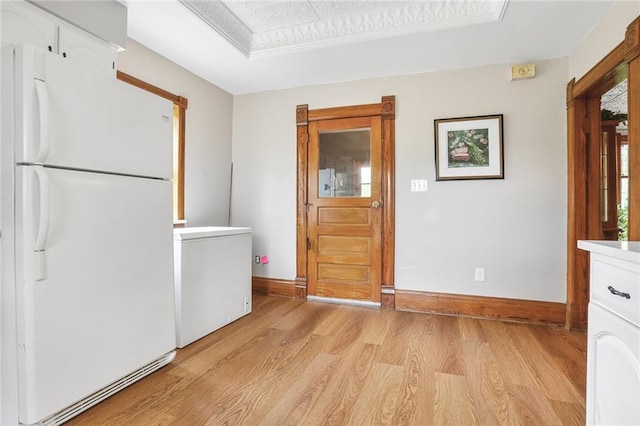 kitchen with freestanding refrigerator, refrigerator, light wood finished floors, a tray ceiling, and baseboards
