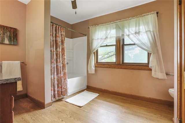 full bath featuring wood finished floors, baseboards, shower / bath combo, and toilet