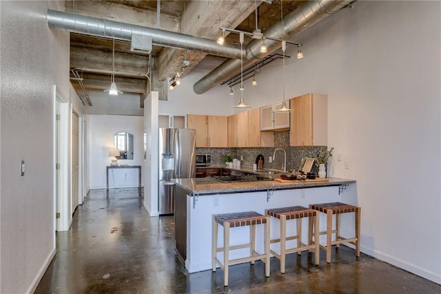 kitchen featuring stainless steel fridge, light brown cabinets, backsplash, a peninsula, and concrete flooring