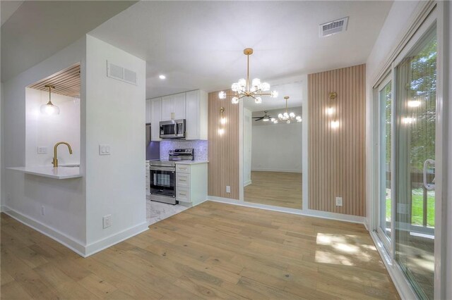 12136 Hayes St, Overland Park, KS 66213 - kitchen with stainless steel appliances, a chandelier, a sink, white cabinets, and light wood-type flooring