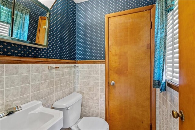 4305 Doctor Greaves Rd, Grandview, MO 64030 - half bathroom with tile walls, wallpapered walls, toilet, a sink, and a wainscoted wall