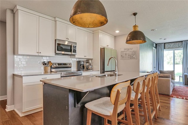 kitchen featuring appliances with stainless steel finishes, light wood-style floors, open floor plan, a sink, and white cabinets