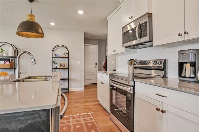 kitchen featuring appliances with stainless steel finishes, a sink, backsplash, light wood-style flooring, and white cabinetry