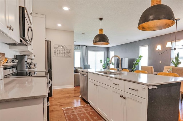 kitchen featuring a sink, appliances with stainless steel finishes, open floor plan, white cabinets, and light wood-type flooring