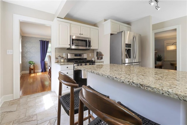 23 W Winthrope Rd, Kansas City, MO 64113 - kitchen with appliances with stainless steel finishes, a breakfast bar, baseboards, light stone counters, and white cabinetry