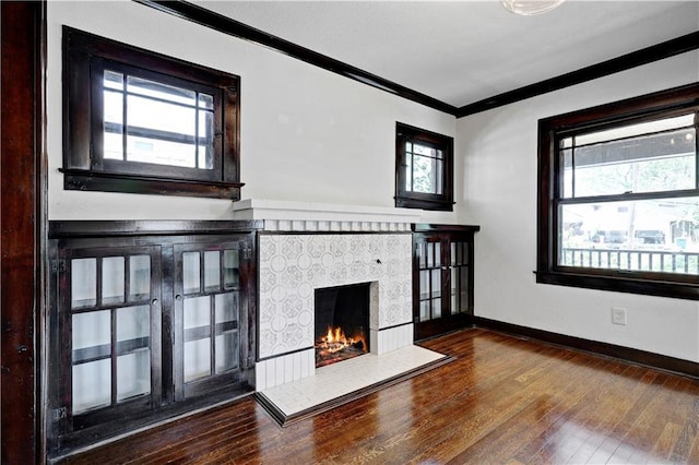 2414 N 12th St, Kansas City, KS 66104 - unfurnished living room with crown molding, a tiled fireplace, hardwood / wood-style flooring, and baseboards