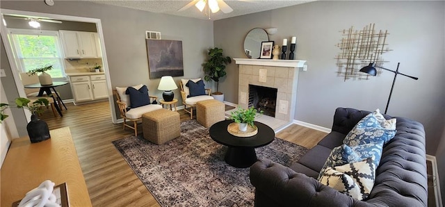 7934 Hemlock St, Overland Park, KS 66204 - living area featuring a ceiling fan, light wood-style floors, a tile fireplace, a textured ceiling, and baseboards