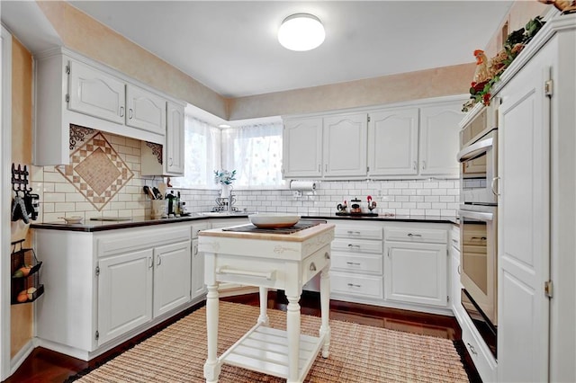 kitchen with dark countertops, white cabinetry, backsplash, and dark wood-style floors