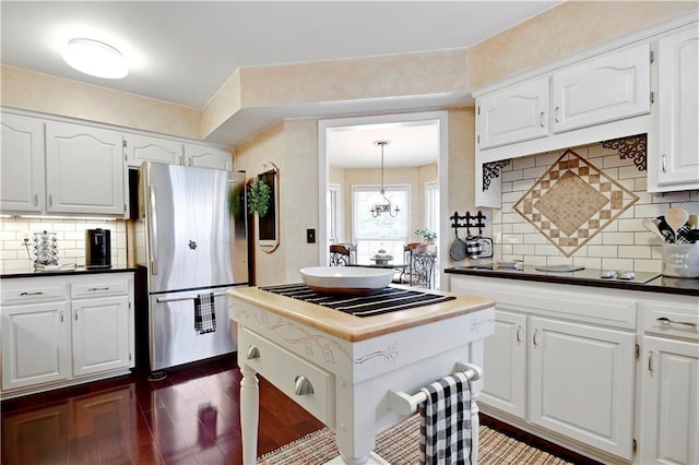 kitchen with freestanding refrigerator, dark countertops, stovetop, white cabinets, and tasteful backsplash