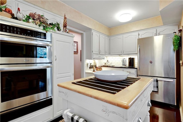 kitchen with stainless steel appliances, tasteful backsplash, white cabinetry, a center island, and dark wood-style flooring