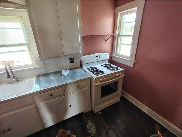 kitchen featuring gas range gas stove, a sink, dark wood-type flooring, stainless steel counters, and baseboards
