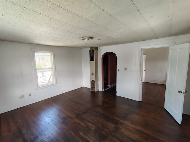 spare room featuring arched walkways and hardwood / wood-style flooring
