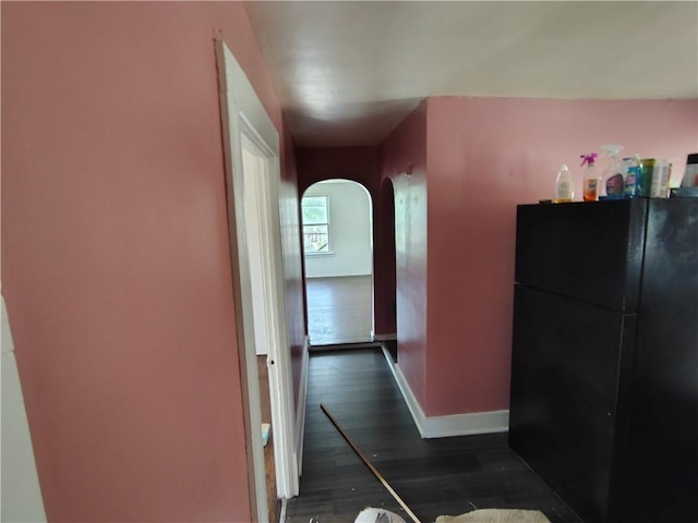 corridor featuring arched walkways, dark wood-style flooring, and baseboards