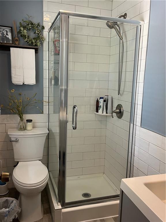 full bath featuring tile walls, a stall shower, toilet, and vanity