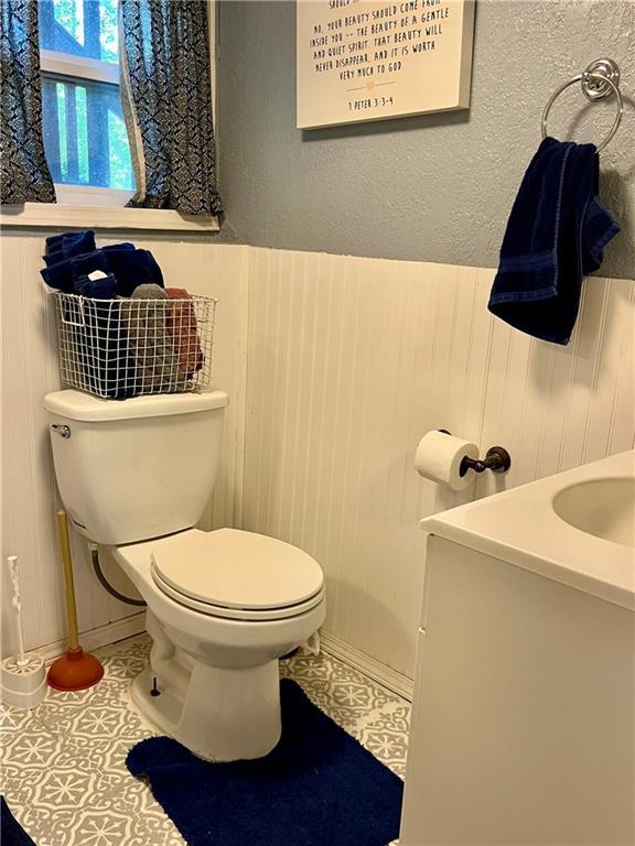 bathroom with a wainscoted wall, toilet, tile patterned floors, vanity, and wood walls