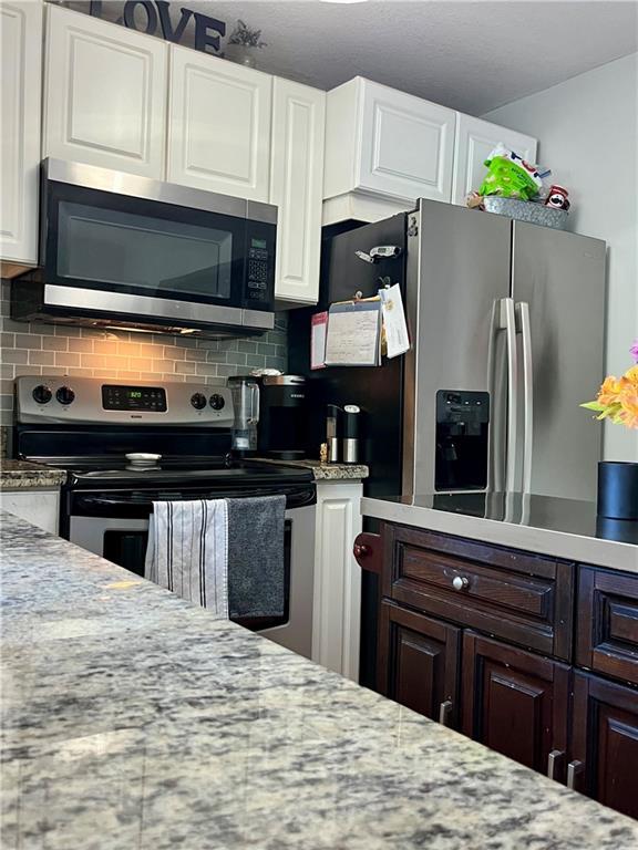 kitchen with stainless steel appliances, backsplash, white cabinets, light stone countertops, and dark brown cabinetry