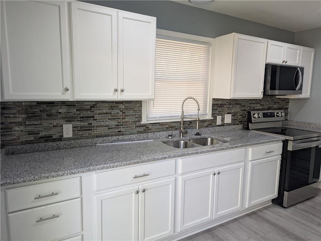 kitchen with appliances with stainless steel finishes, a sink, white cabinetry, tasteful backsplash, and light stone counters