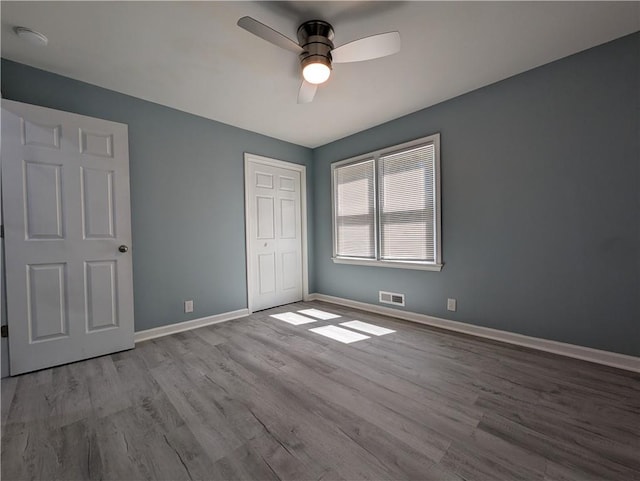 unfurnished bedroom with wood finished floors, baseboards, a closet, and a ceiling fan
