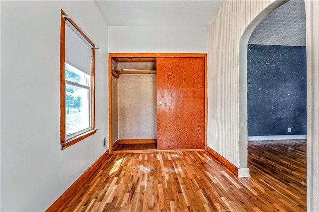 218 S 8th St, Kansas City, KS 66101 - unfurnished bedroom featuring wood-type flooring, wallpapered walls, baseboards, arched walkways, and a closet