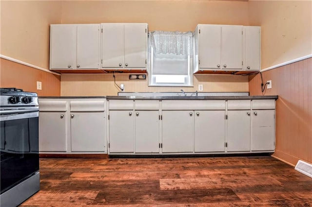 218 S 8th St, Kansas City, KS 66101 - kitchen featuring stainless steel gas range oven, white cabinets, dark wood-style flooring, dark countertops, and wainscoting