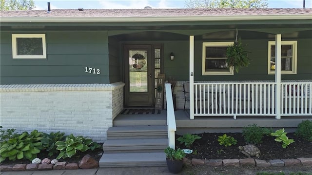 view of exterior entry with a porch and brick siding