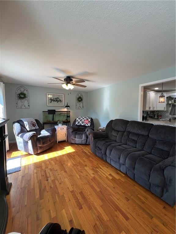 living room with light wood-style flooring, ceiling fan, and a textured ceiling