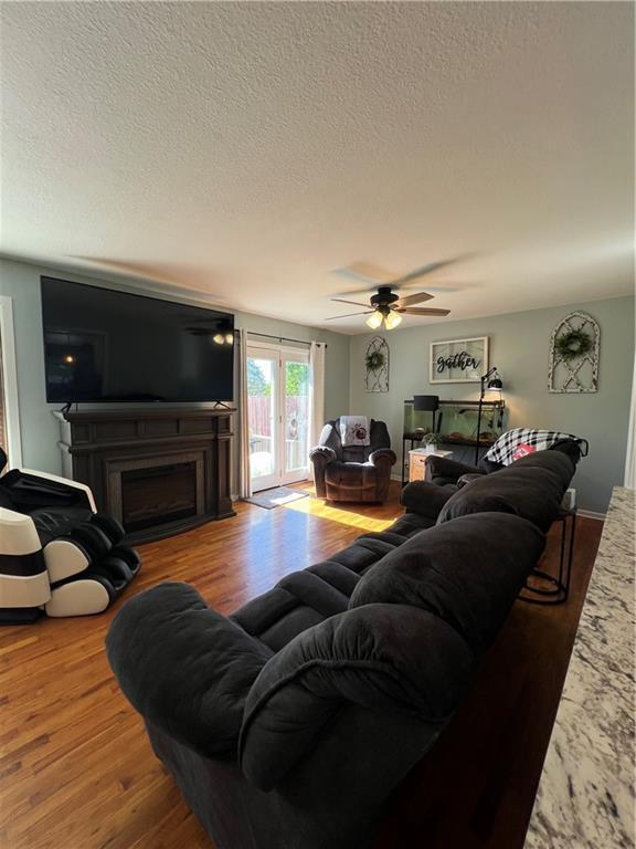 living area featuring a textured ceiling, wood finished floors, ceiling fan, and a fireplace