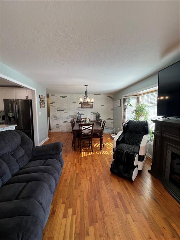 living area with light wood finished floors, a chandelier, a textured ceiling, brick wall, and baseboards