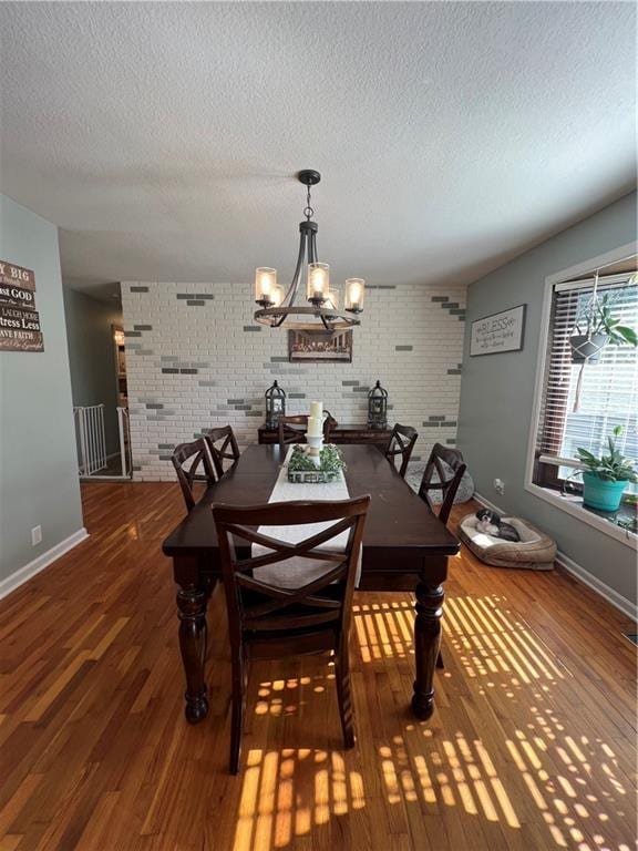 dining room with a textured ceiling, wood finished floors, a chandelier, baseboards, and brick wall
