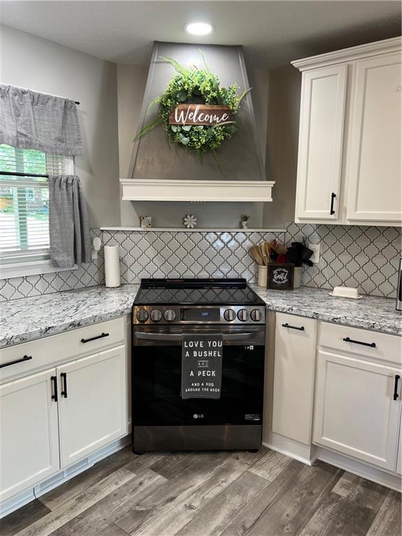 kitchen featuring stainless steel electric range oven, custom exhaust hood, tasteful backsplash, light wood-style floors, and white cabinetry