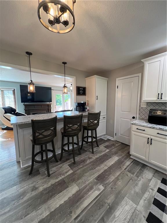 kitchen featuring healthy amount of natural light, white cabinets, dark wood-type flooring, a breakfast bar, and a textured ceiling