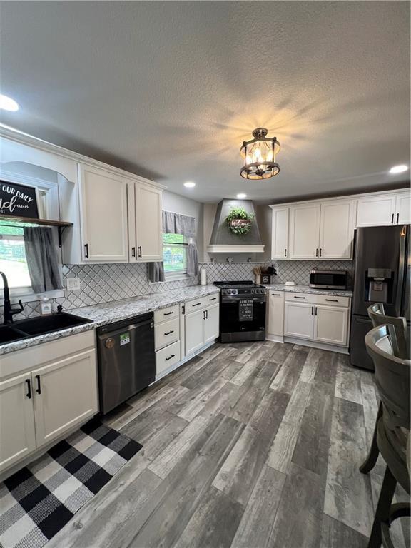 kitchen with electric range, dishwashing machine, black fridge, wall chimney exhaust hood, and stainless steel microwave