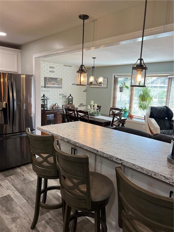 kitchen with stainless steel fridge, a kitchen breakfast bar, white cabinetry, light wood finished floors, and a textured ceiling