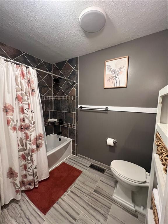 bathroom featuring a textured ceiling, toilet, and shower / tub combo with curtain