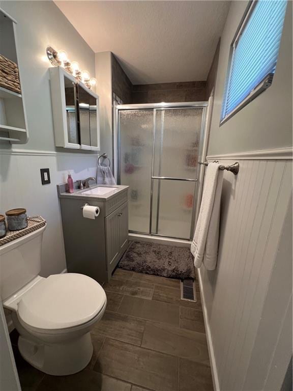 bathroom with vanity, a shower stall, toilet, wainscoting, and a textured ceiling