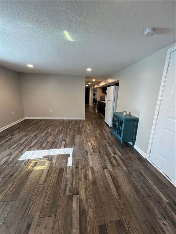 unfurnished living room featuring dark wood-type flooring, a textured ceiling, recessed lighting, and baseboards
