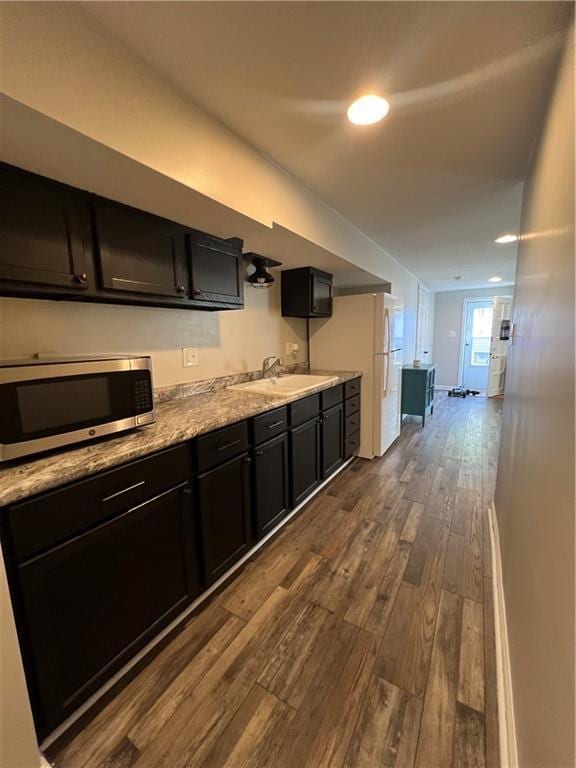 kitchen with stainless steel microwave, a sink, dark wood finished floors, dark cabinetry, and recessed lighting