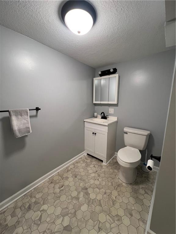 bathroom with a textured ceiling, toilet, vanity, and baseboards