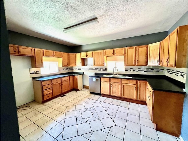 kitchen with dishwasher, a sink, a textured ceiling, light tile patterned floors, and dark countertops