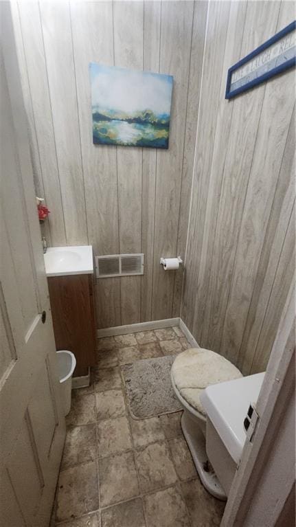 half bath featuring stone finish flooring, toilet, vanity, wood walls, and baseboards