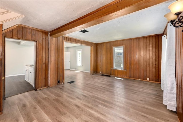 2409 Oakley Ave, Kansas City, MO 64127 - unfurnished living room with light wood finished floors, wood walls, baseboards, a textured ceiling, and beam ceiling
