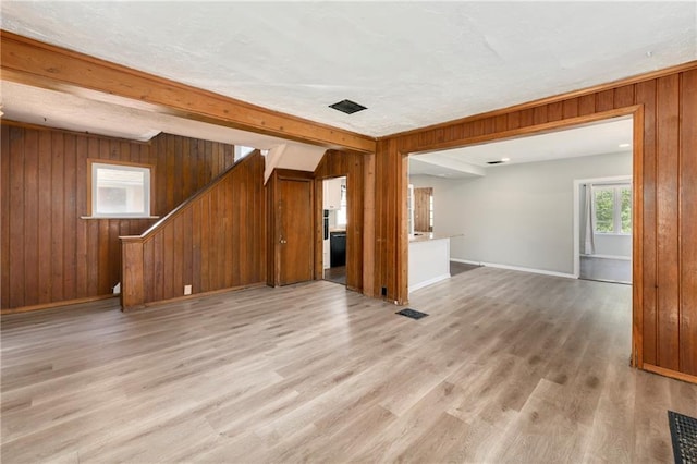 2409 Oakley Ave, Kansas City, MO 64127 - unfurnished living room featuring stairs, wood walls, light wood-type flooring, baseboards, and beamed ceiling