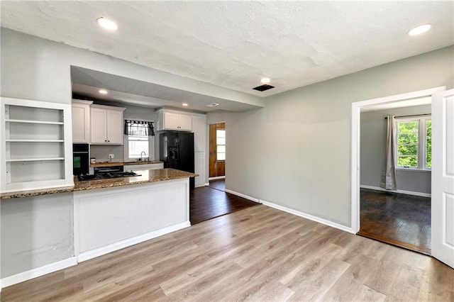 2409 Oakley Ave, Kansas City, MO 64127 - kitchen with white cabinetry, light wood-style floors, black refrigerator with ice dispenser, dark stone counters, and recessed lighting