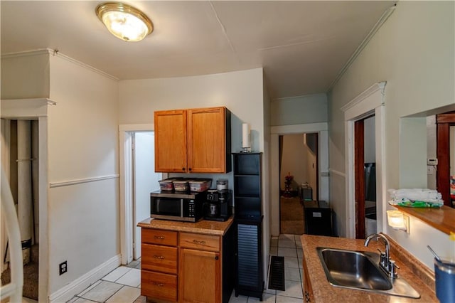 911 N 6th St, Atchison, KS 66002 - kitchen with a sink, stainless steel microwave, light tile patterned floors, brown cabinets, and ornamental molding